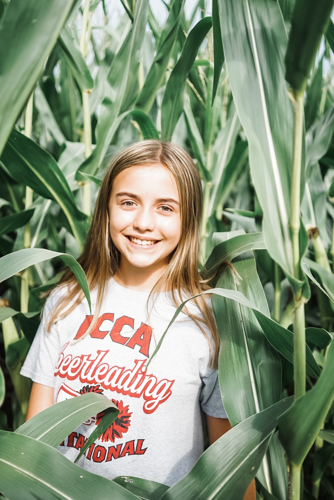 Girl standing in corn field smiling at camera. 