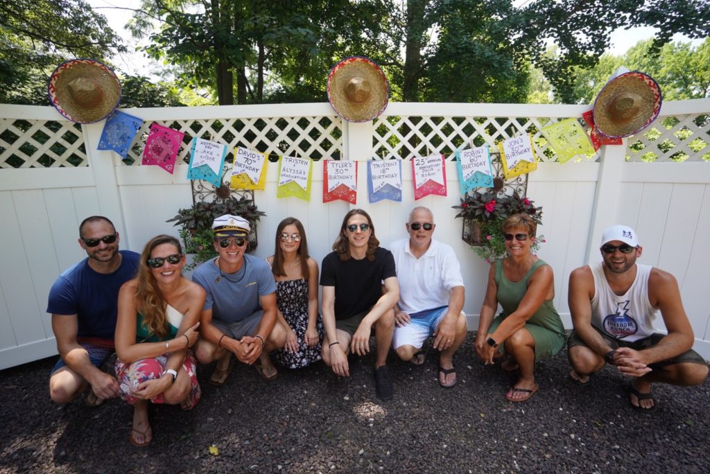 Group of nine people squatting in front of a banner smiling at camera. The banner reads nine messages on birthdays, anniversaries, and graduations. 
