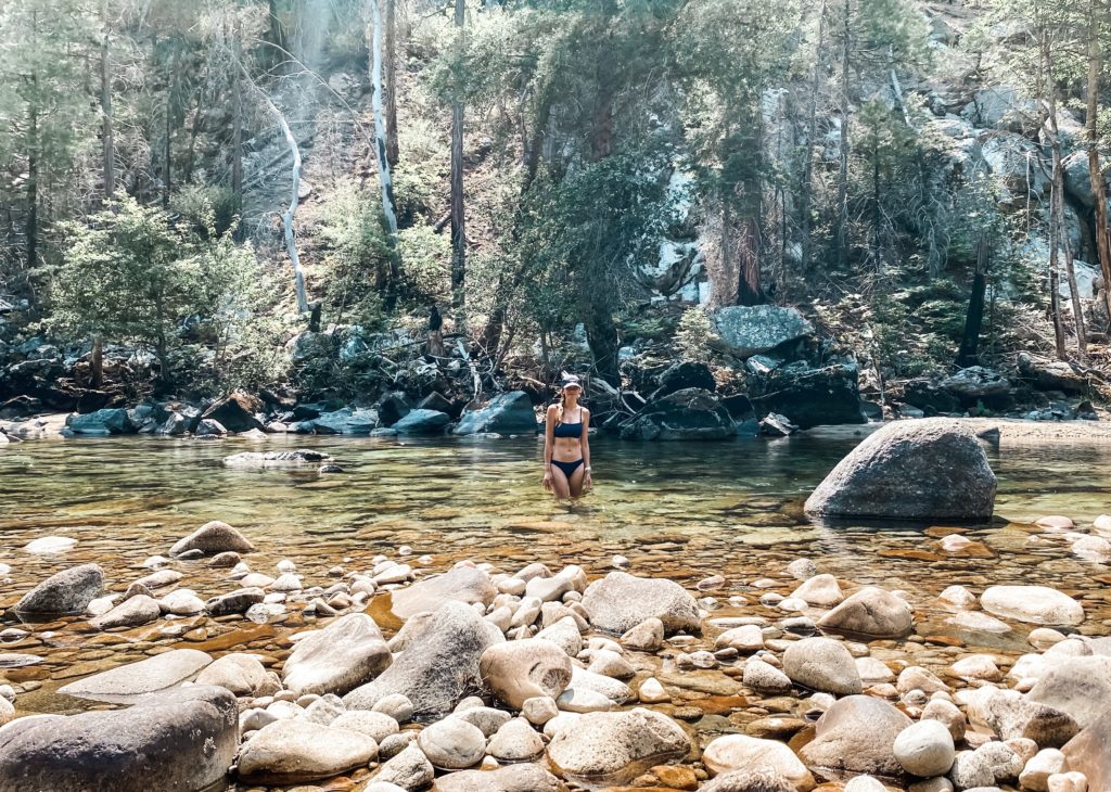 woman standing in clear water of a river with stones in forefront of picture