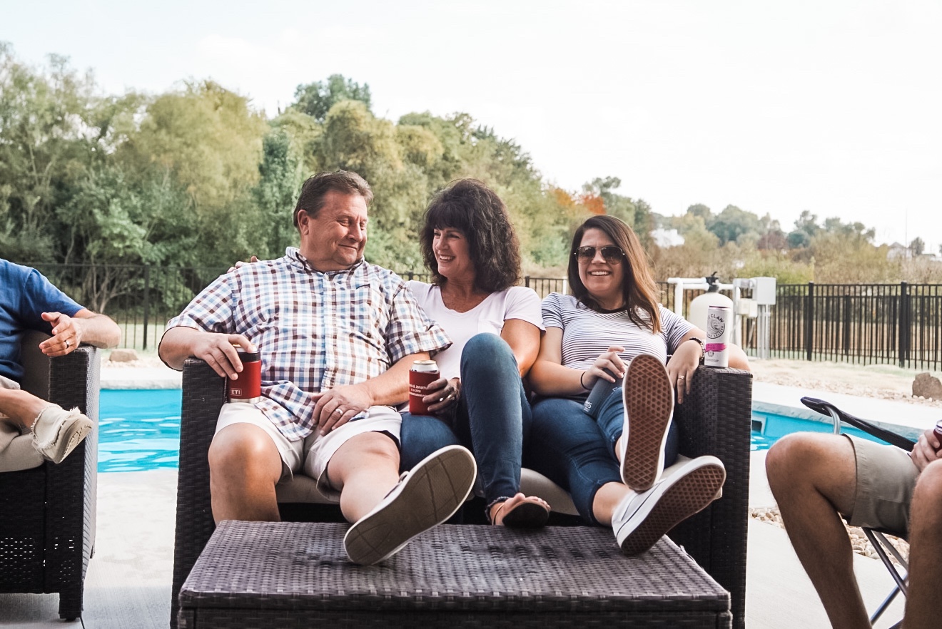 Three people, a man and two women sitting on an outdoor couch laughing